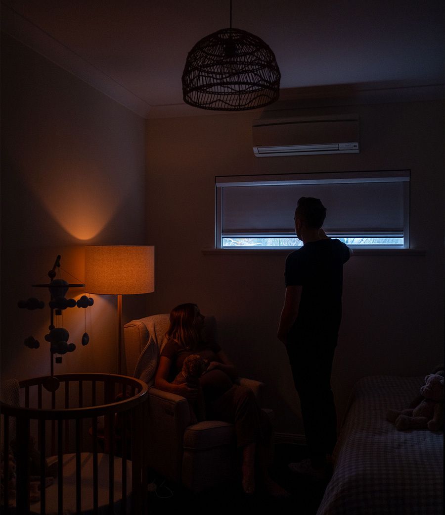 Parents in dark nursery with UBlockout shades creating complete blackout environment for baby sleep