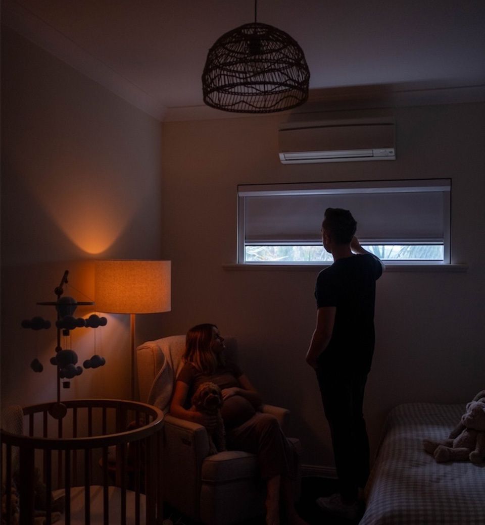 Tired parents in dimly lit nursery at night with light leaking through window blind
