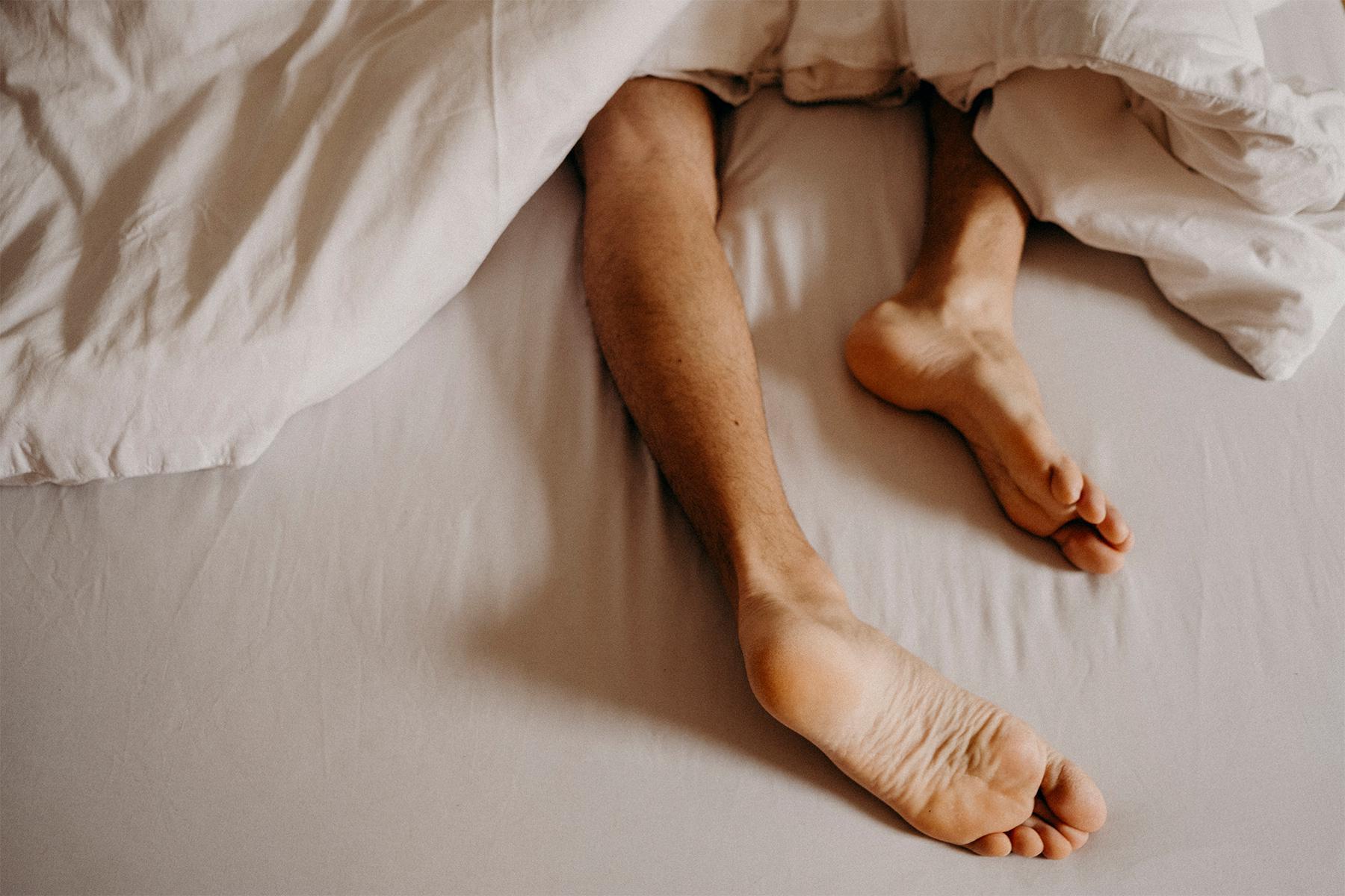 Man's feet sticking out from blankets at the end of a bed.
