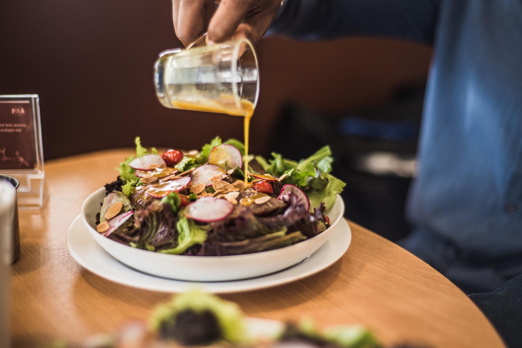 Pouring apple cider vinaigrette onto bowl of salad.