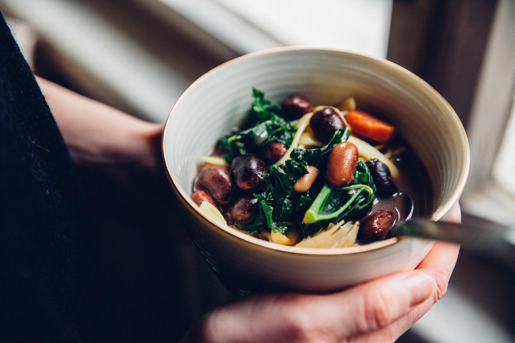 Close-up of hands holding a bowl filled with vegetable soup.