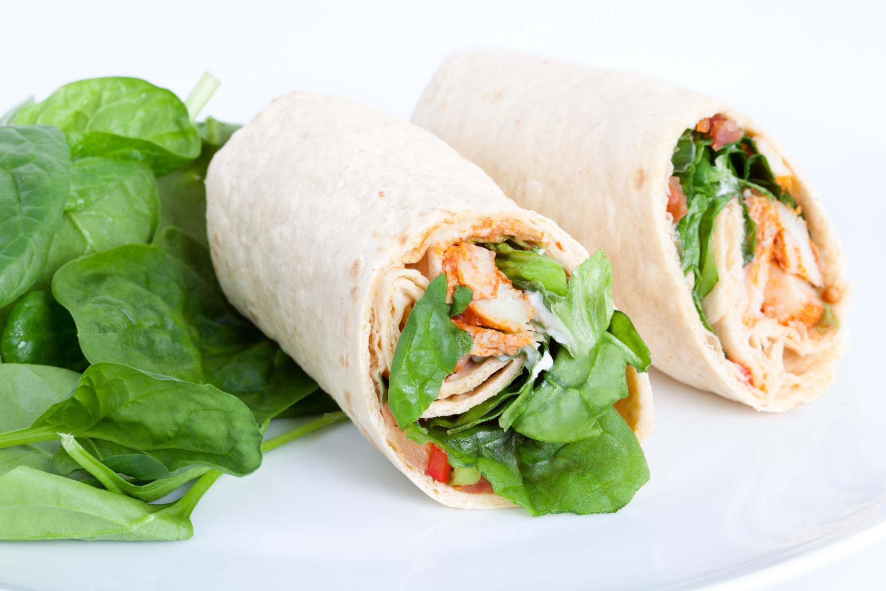 Two smoked chicken wraps on a white plate with a side salad.
