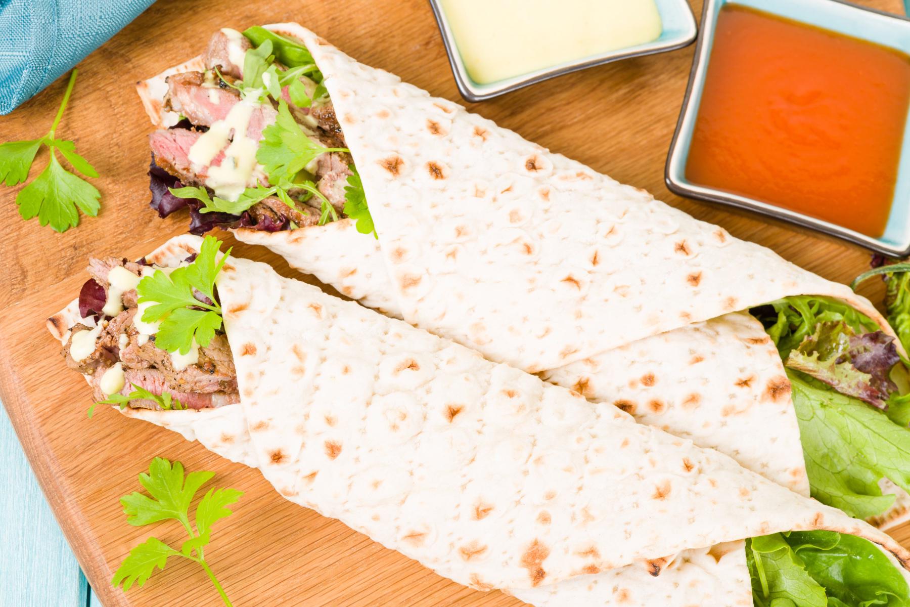 Overhead view of two steaks and bleu cheese wrap on a wooden dish with a dipping sauce.
