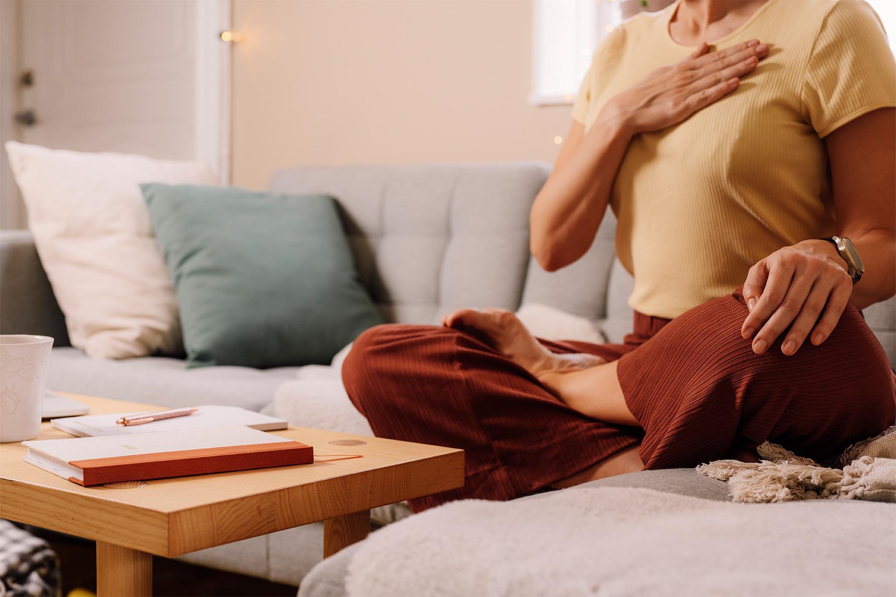 Woman sitting on couch with hand on heart.