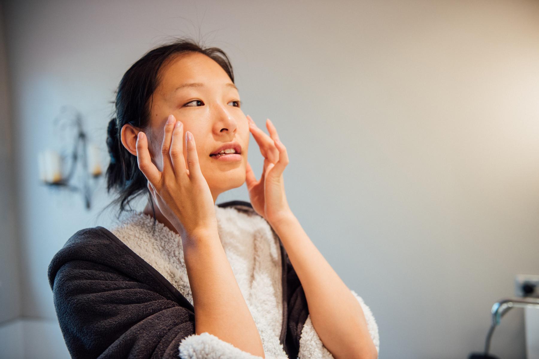 Woman in a robe looking at her face in the mirror.