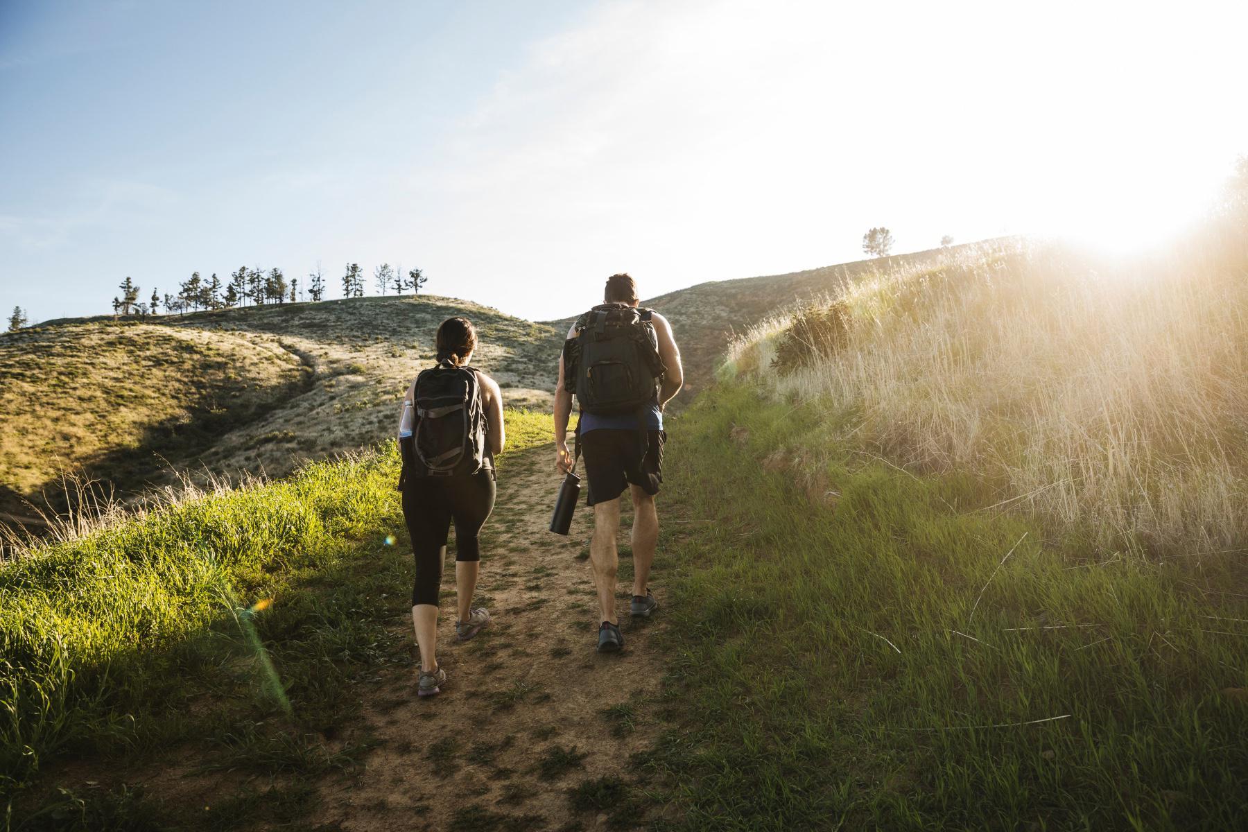 Man and woman with backpacks on hiking up hill.