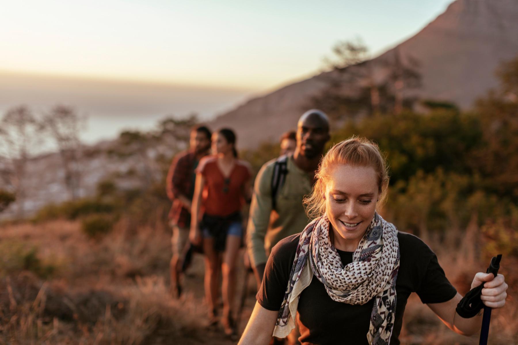 Red-haired woman leading a group of three men and two women on a hike up a mountain during sunset.