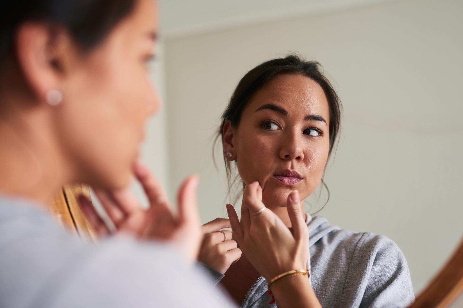 Woman looking at her skin in the bathroom mirror.