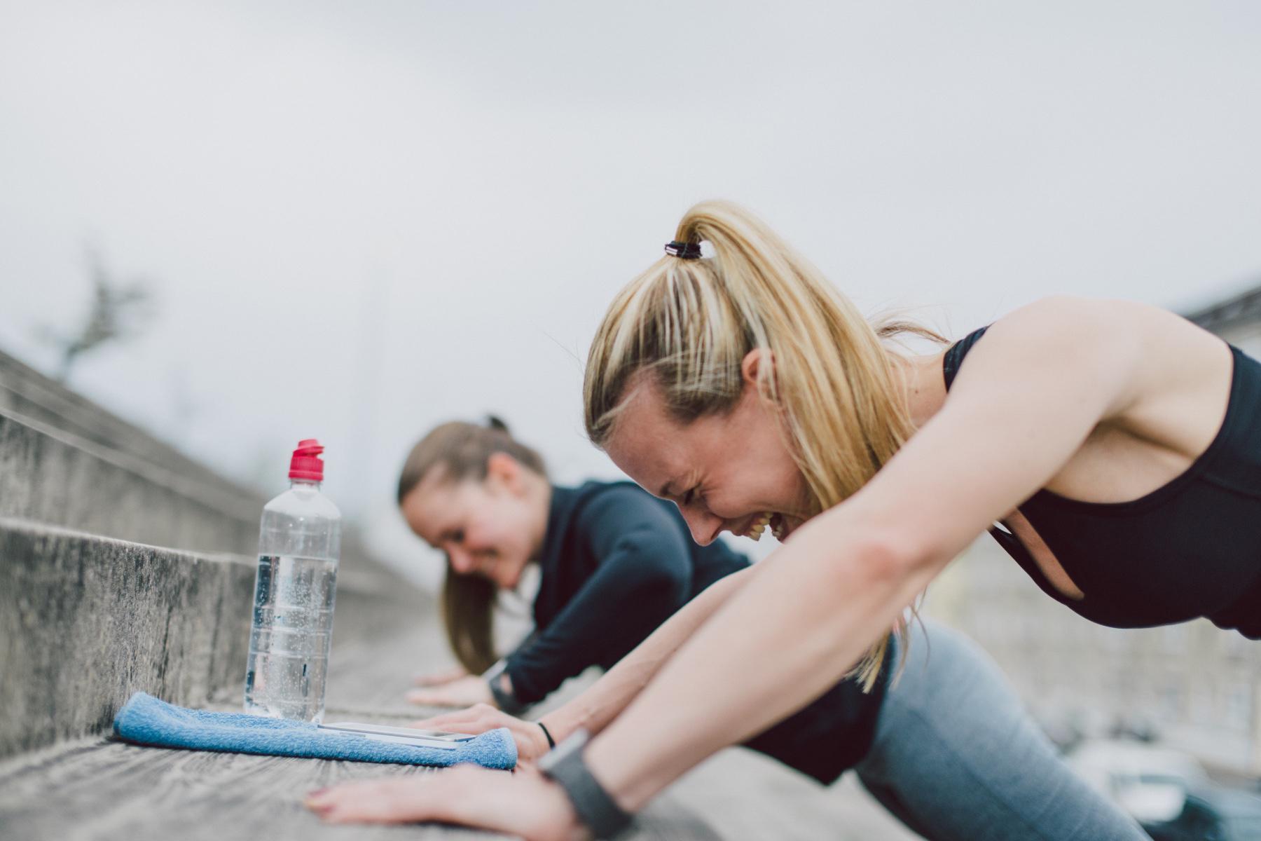 two women laughing while doing push-ups on cement steps outside