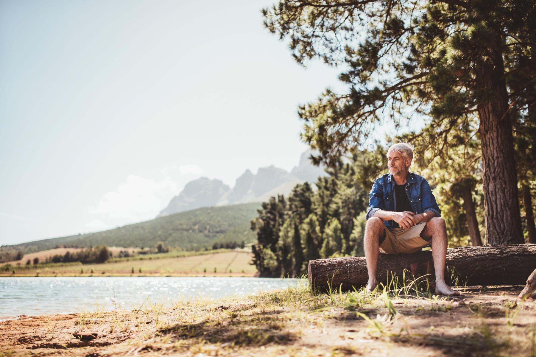 Mature man sitting near a lake looking out into the distance.