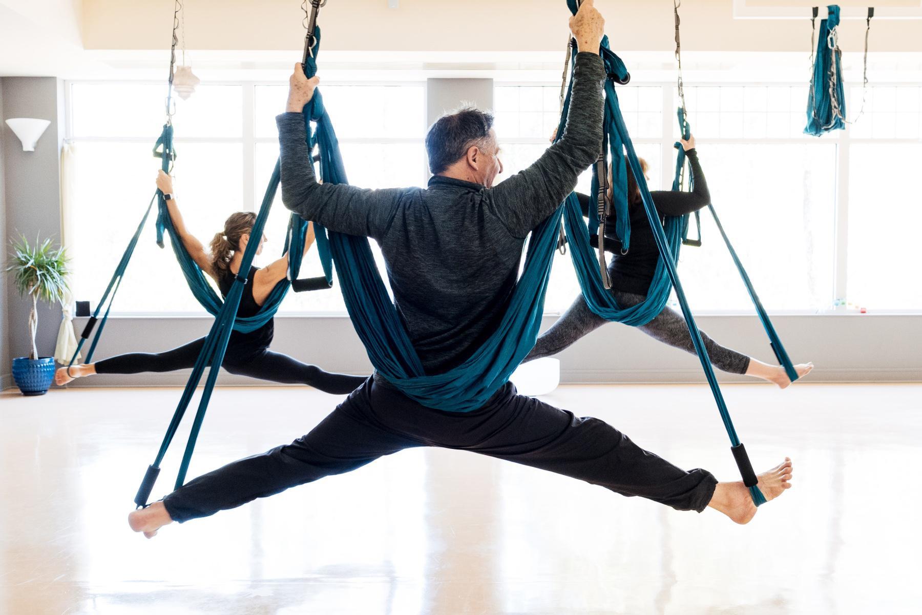 three adults beginning to do a split while in aerial yoga hammocks