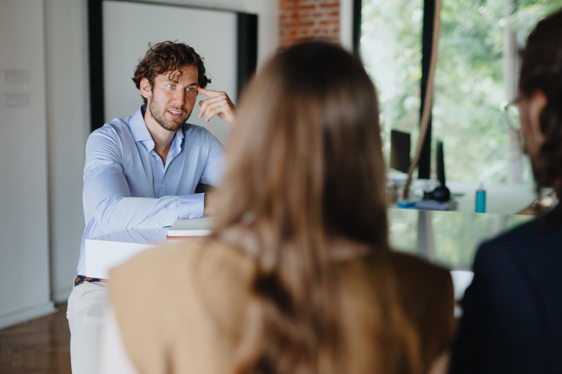 A young man speaking with two female coworkers.