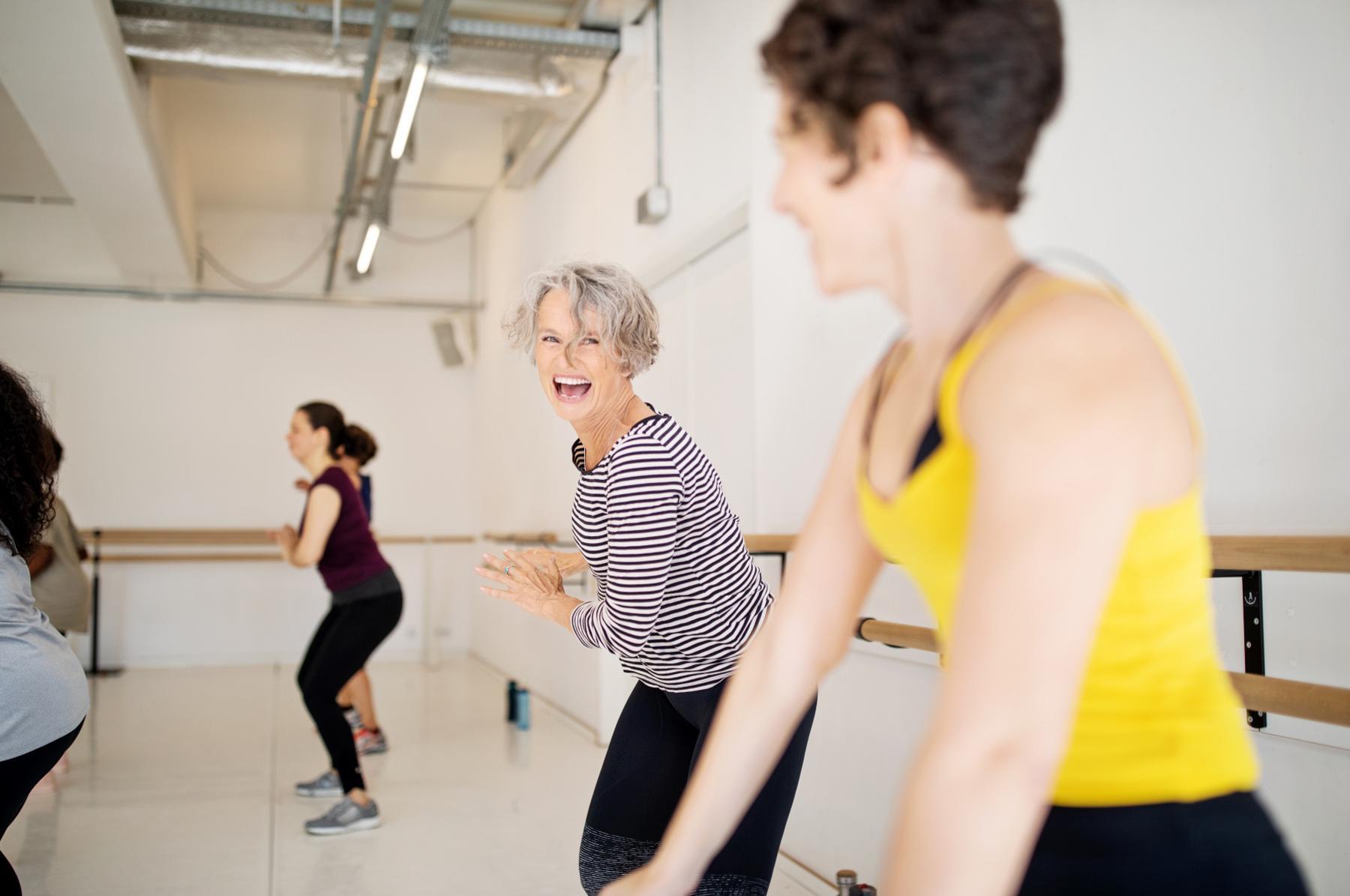 Close-up of two older women in a dance class of six people laughing in movement.