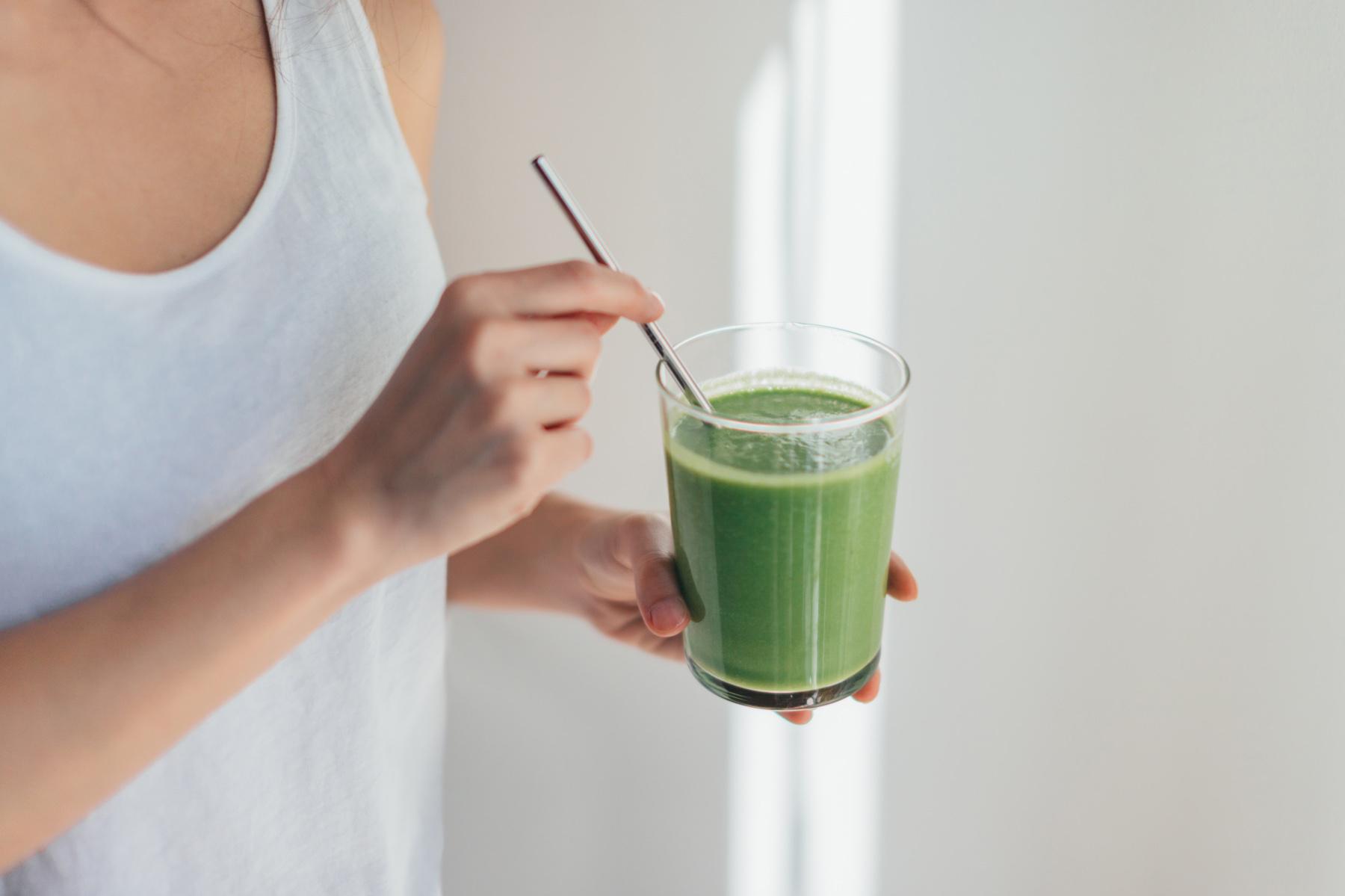 Woman drinking green smoothie in glass with metal straw.