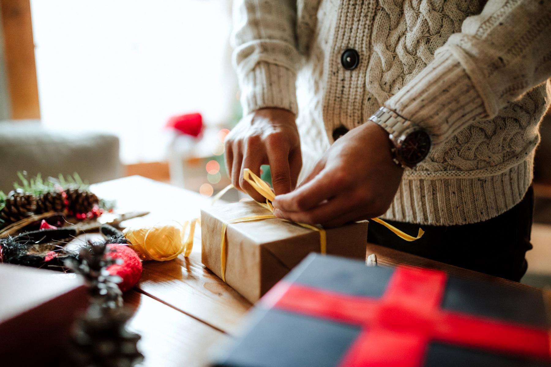 Close-up man wrapping present in brown paper with a yellow bow.