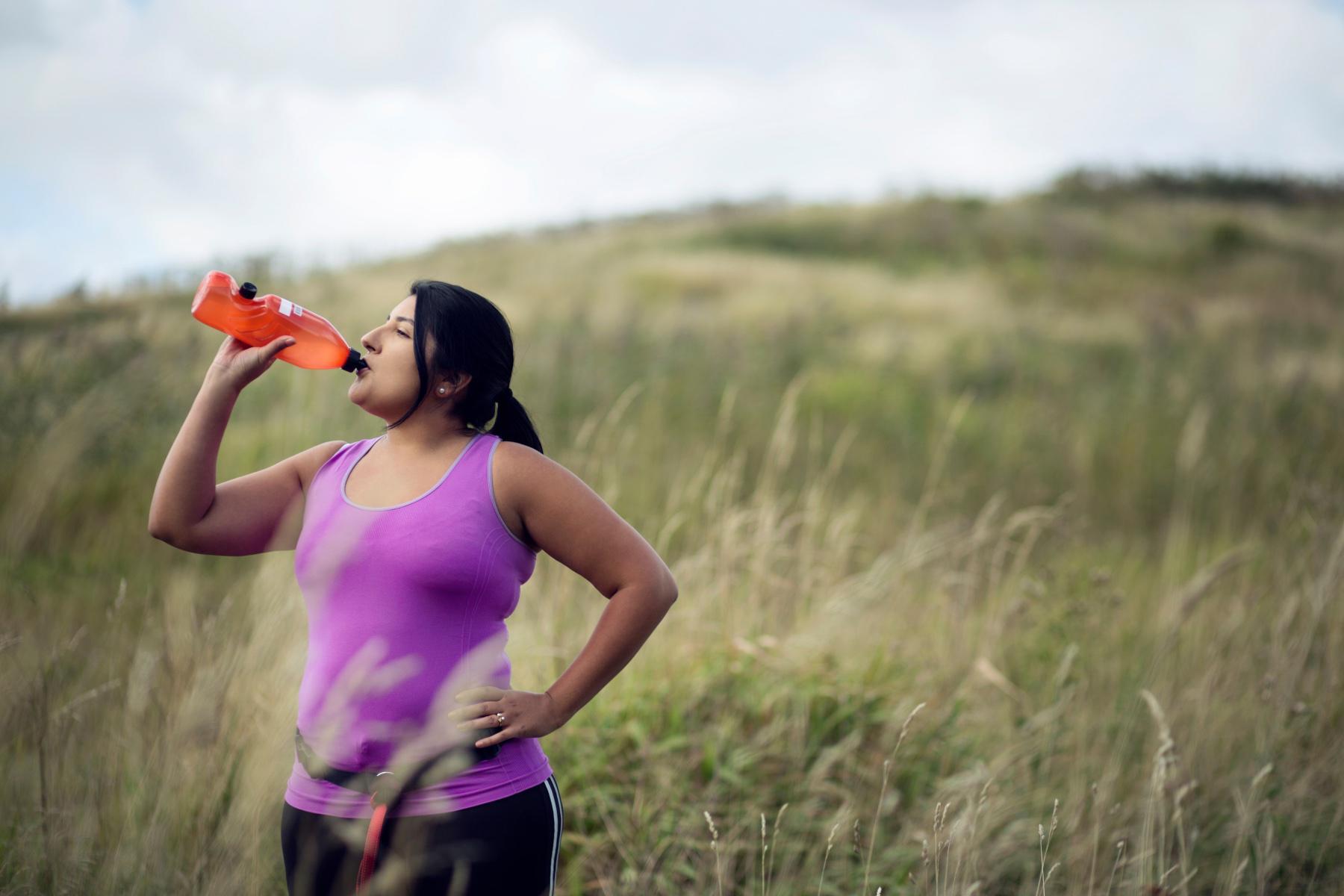 woman outside drinking from water bottle after finishing workout