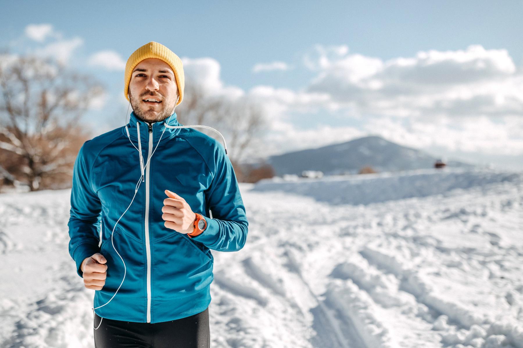 man in blue coat and yellow hat running in snow with headphones on