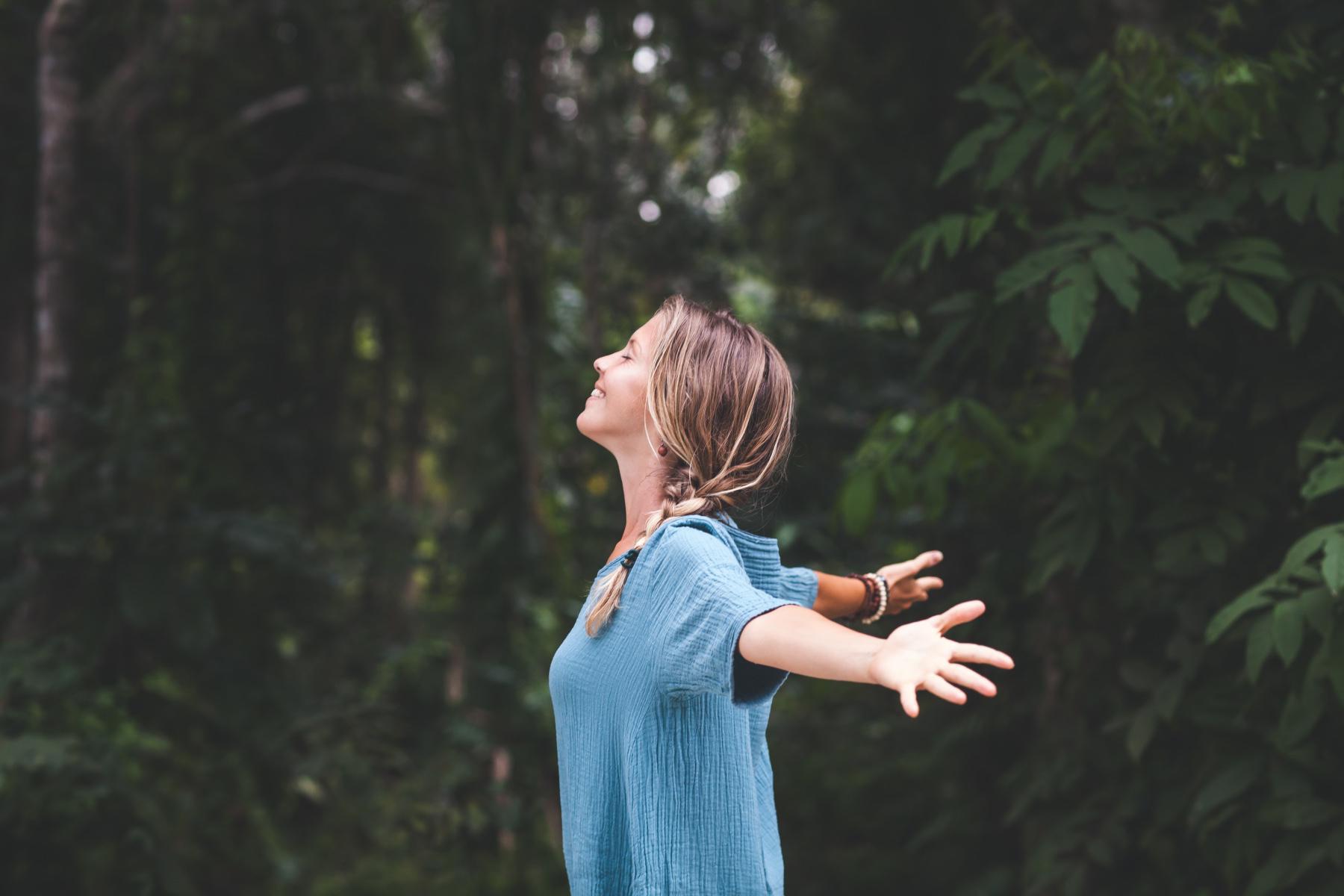 Woman standing in the forest and looking up at the sky.