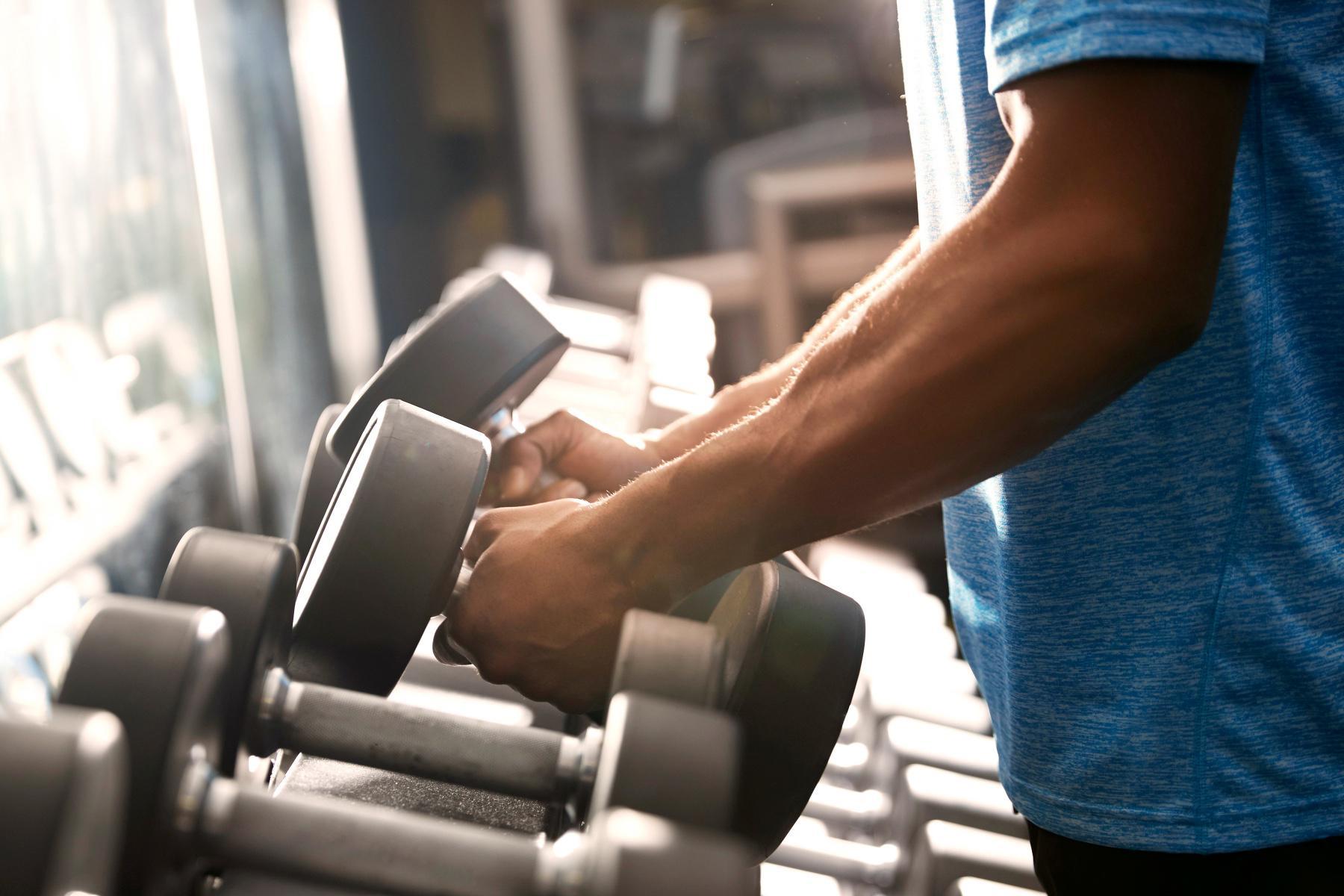 close-up side view of man from shoulders down grabbing dumbbells from rack