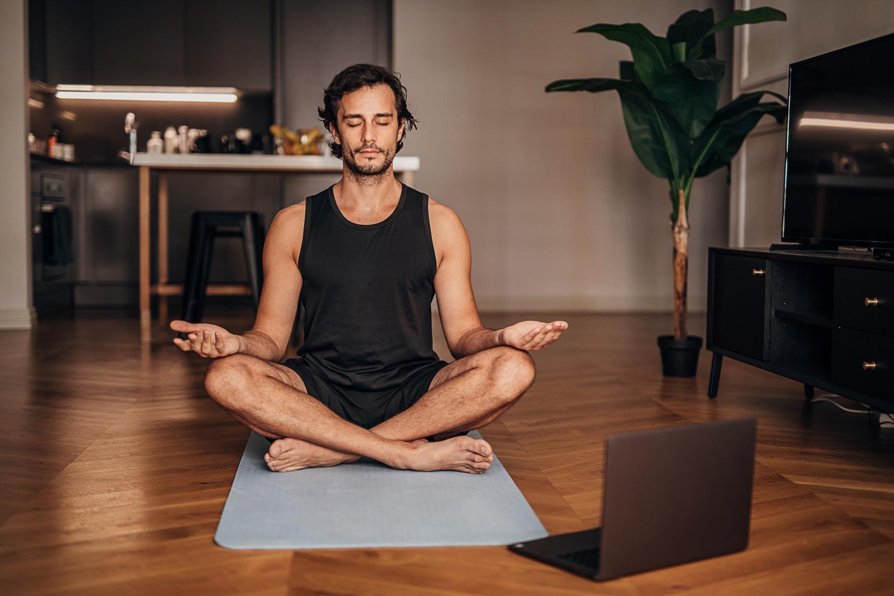 man mediating on yoga mat with computer in front of him