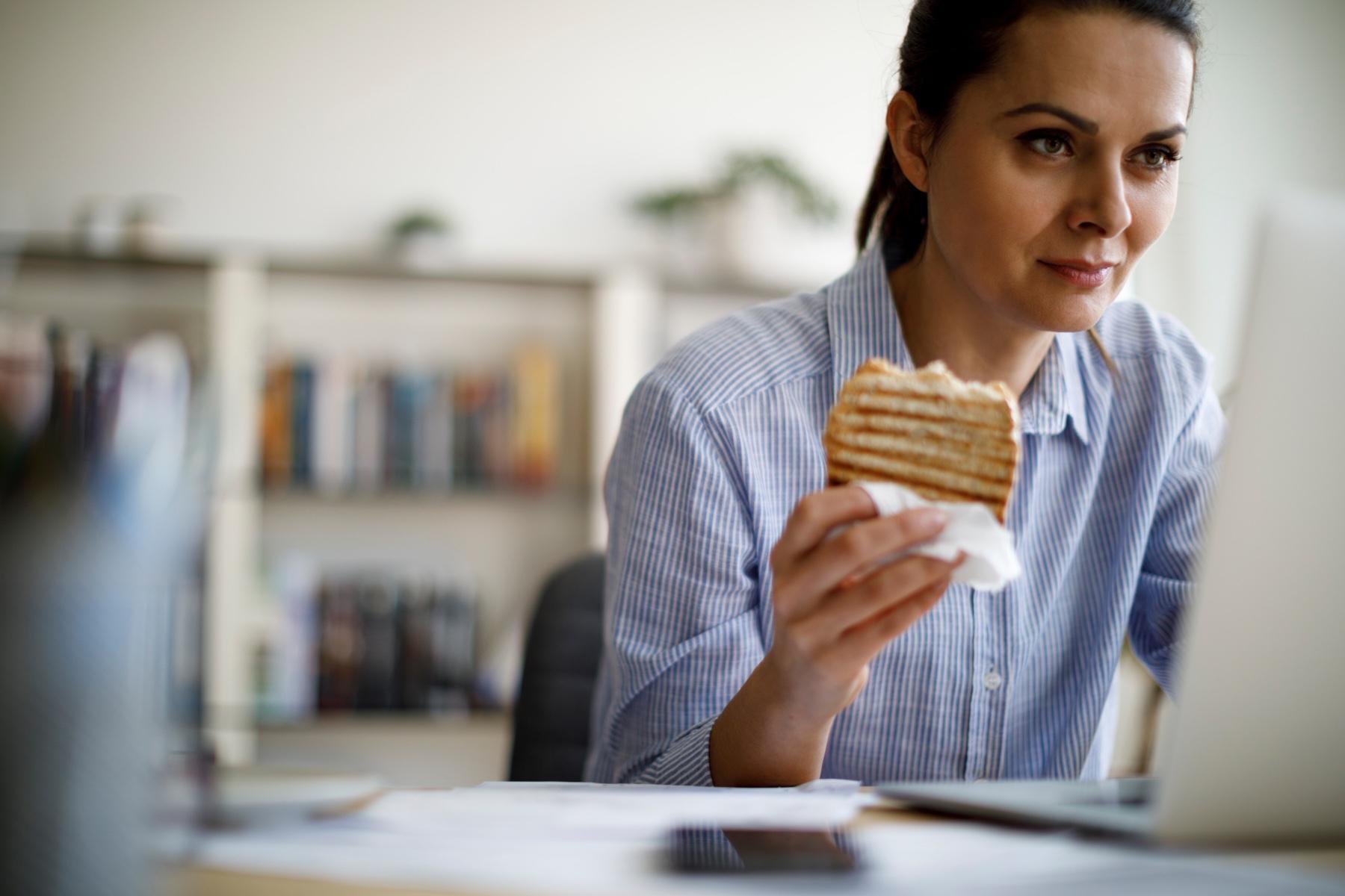 woman eating sandwich while working on laptop