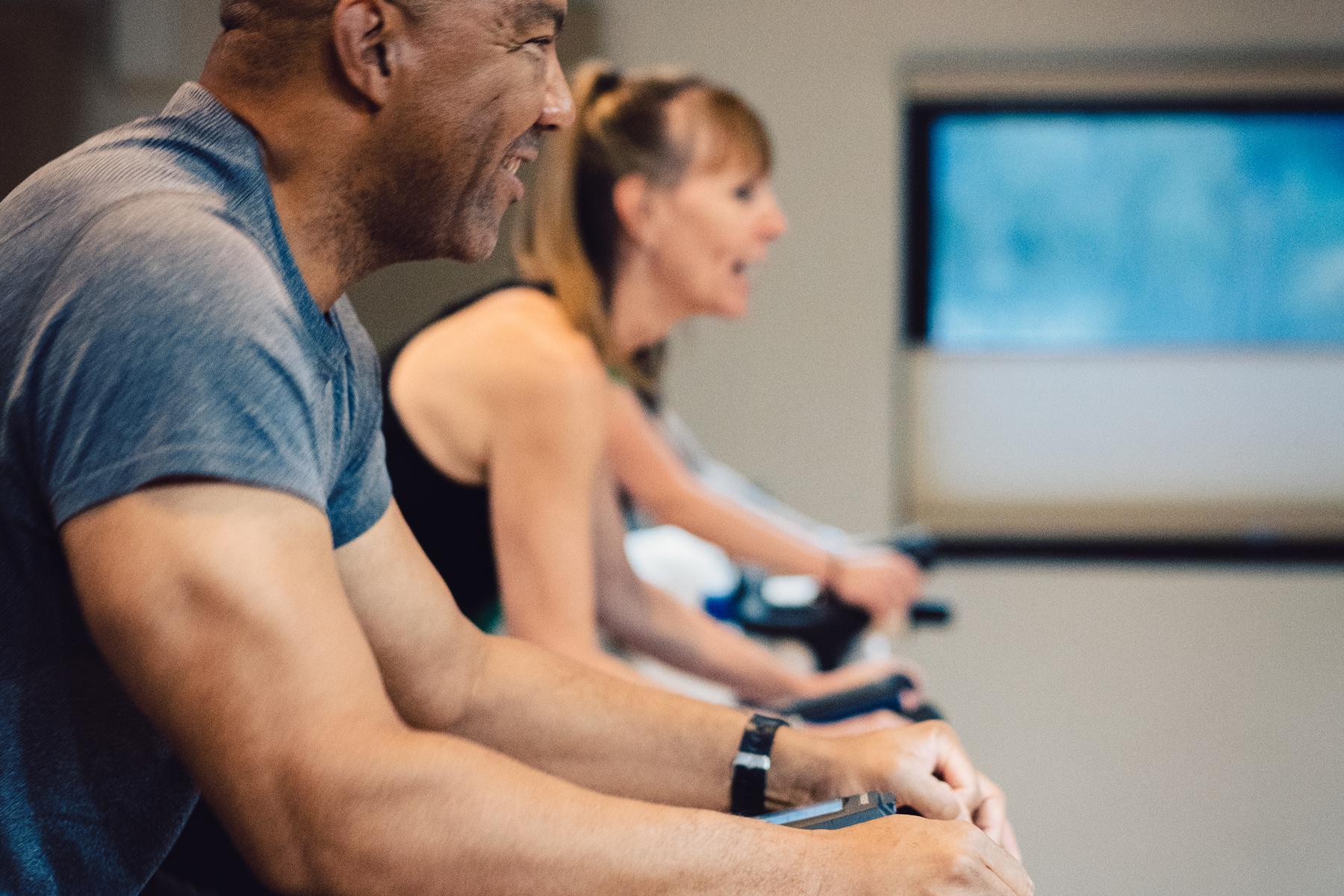 close-up of a man and woman on indoor cycling bikes next to each other