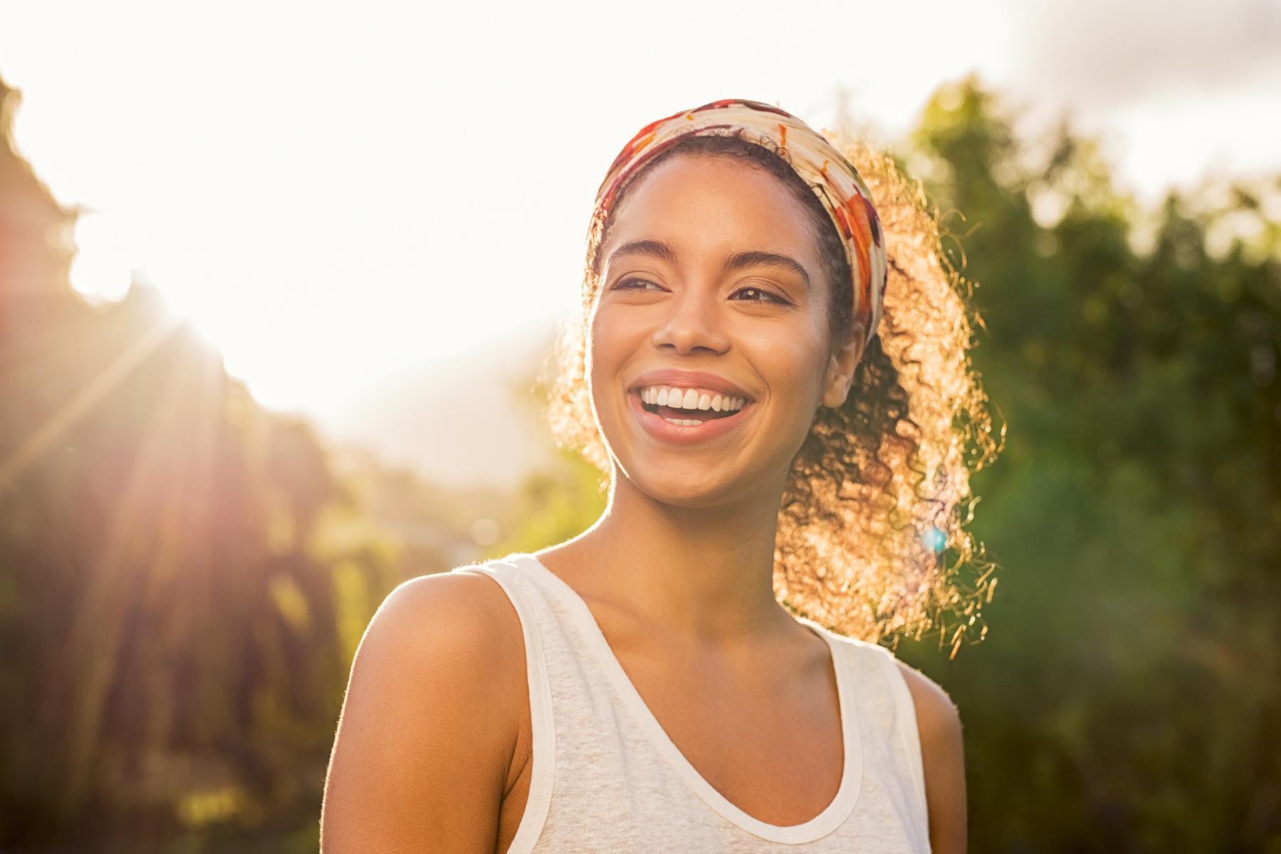 A young woman smiling with the sun behind her.