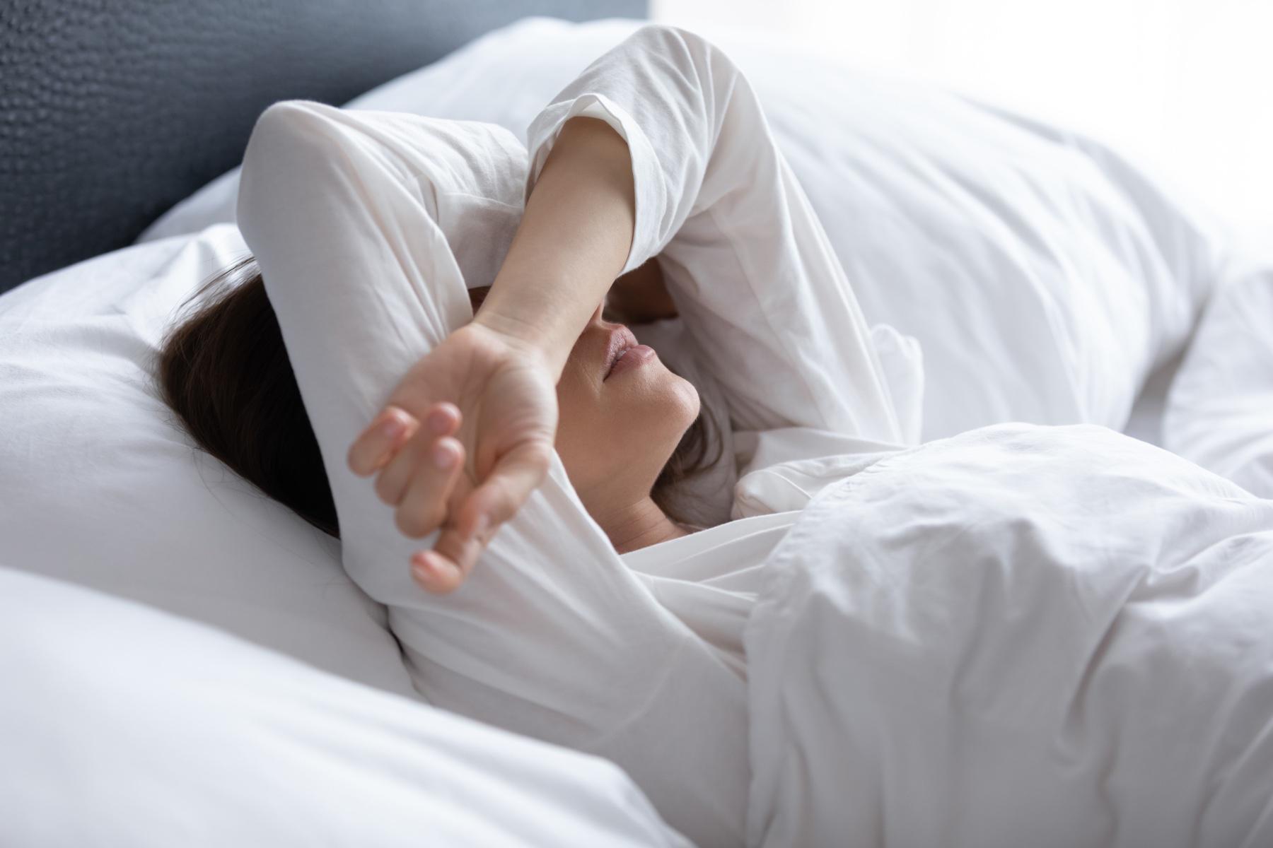 Woman laying in bed with arms over eyes.