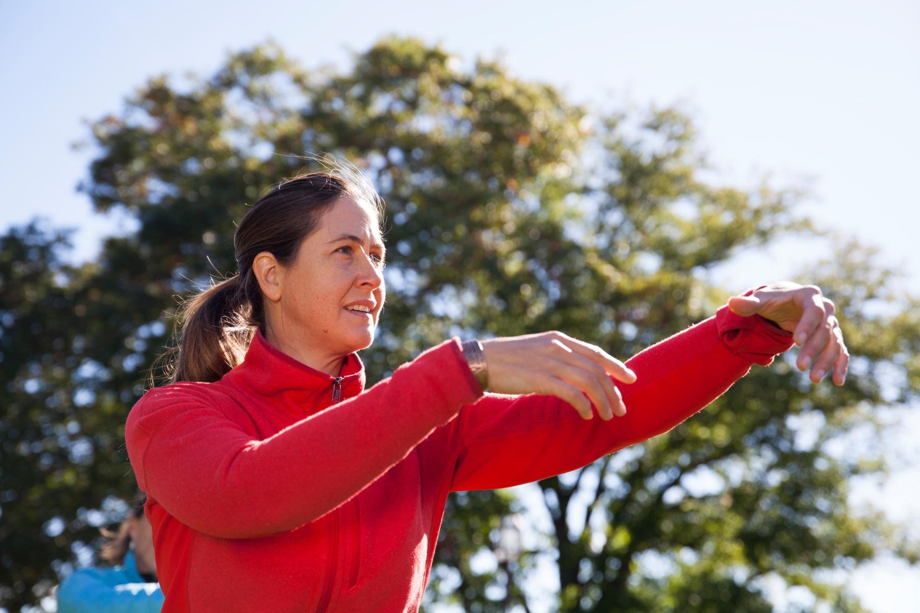woman from waist up wearing a red a jacket with arms up doing qi gong