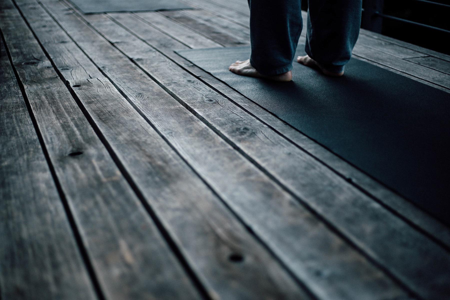 close-up of feet standing on yoga mat on wooden deck