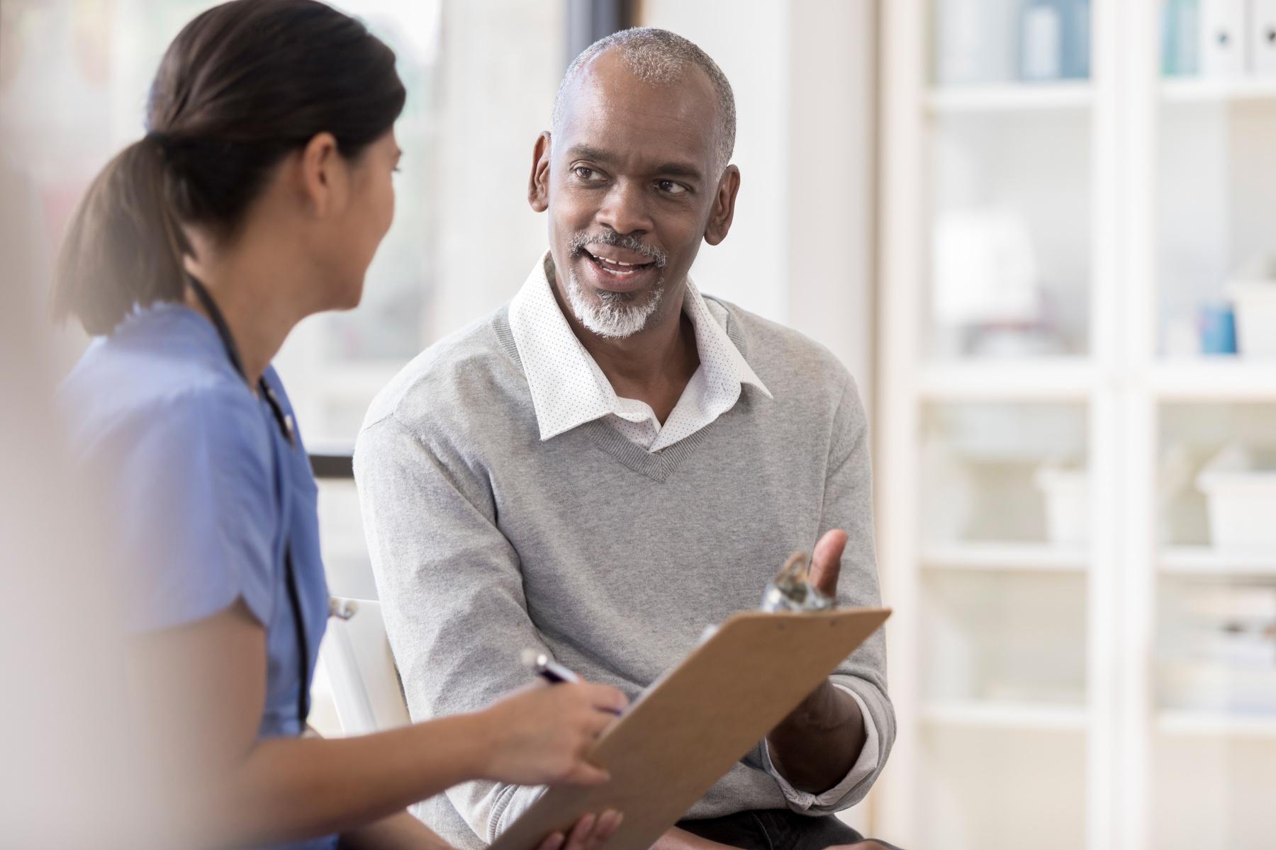 Older man having a conversation with a doctor about results on clipboard in front of them.