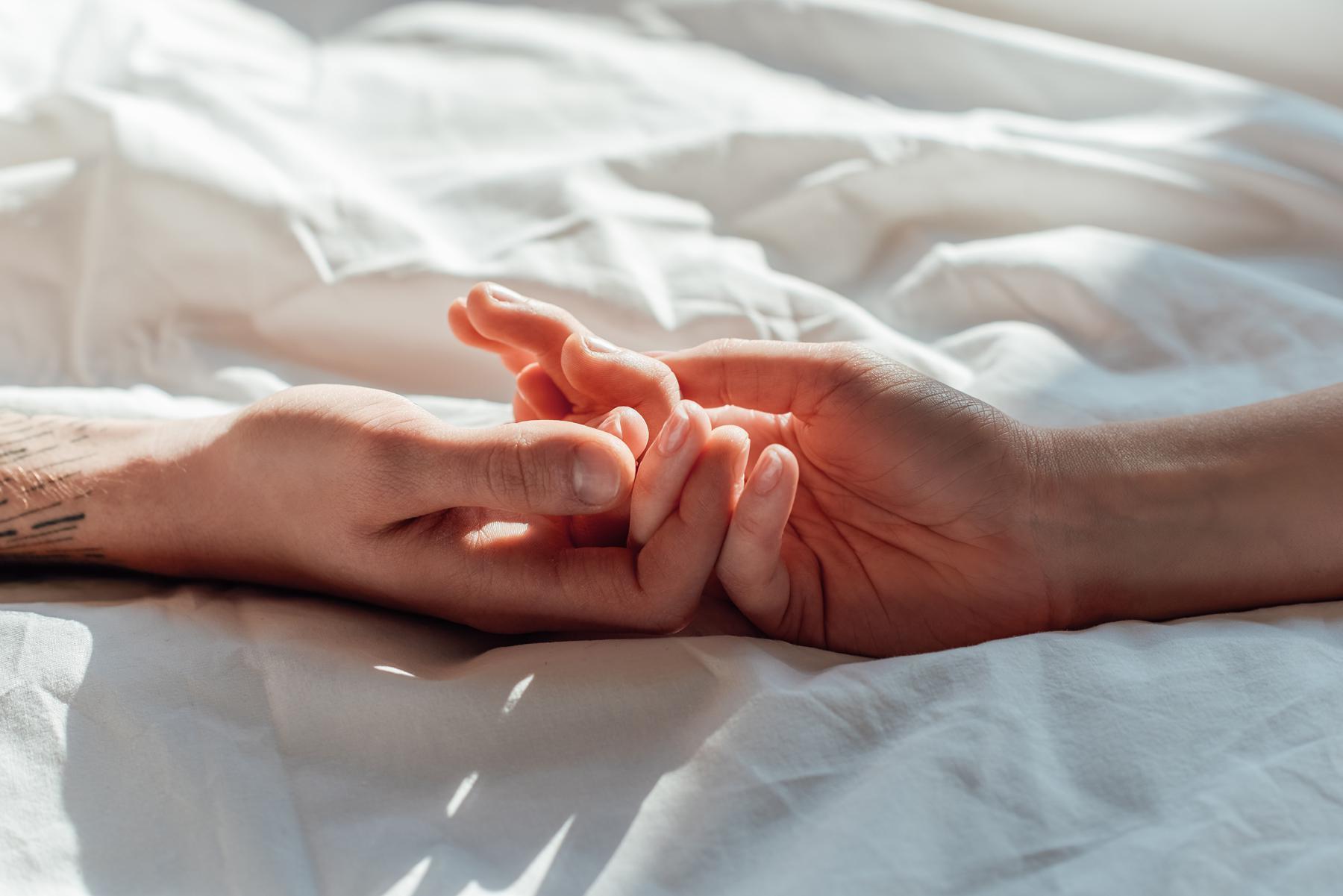 two hands touching on a bed