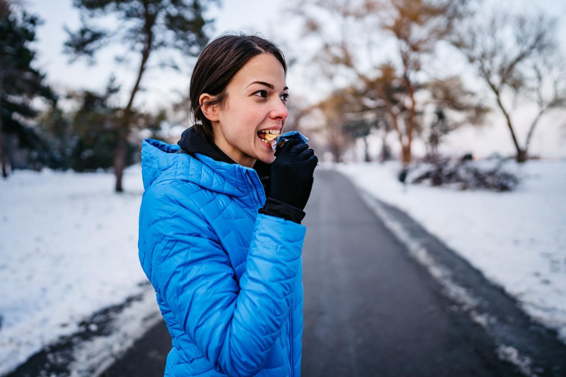 woman eating energy bar on winter trail
