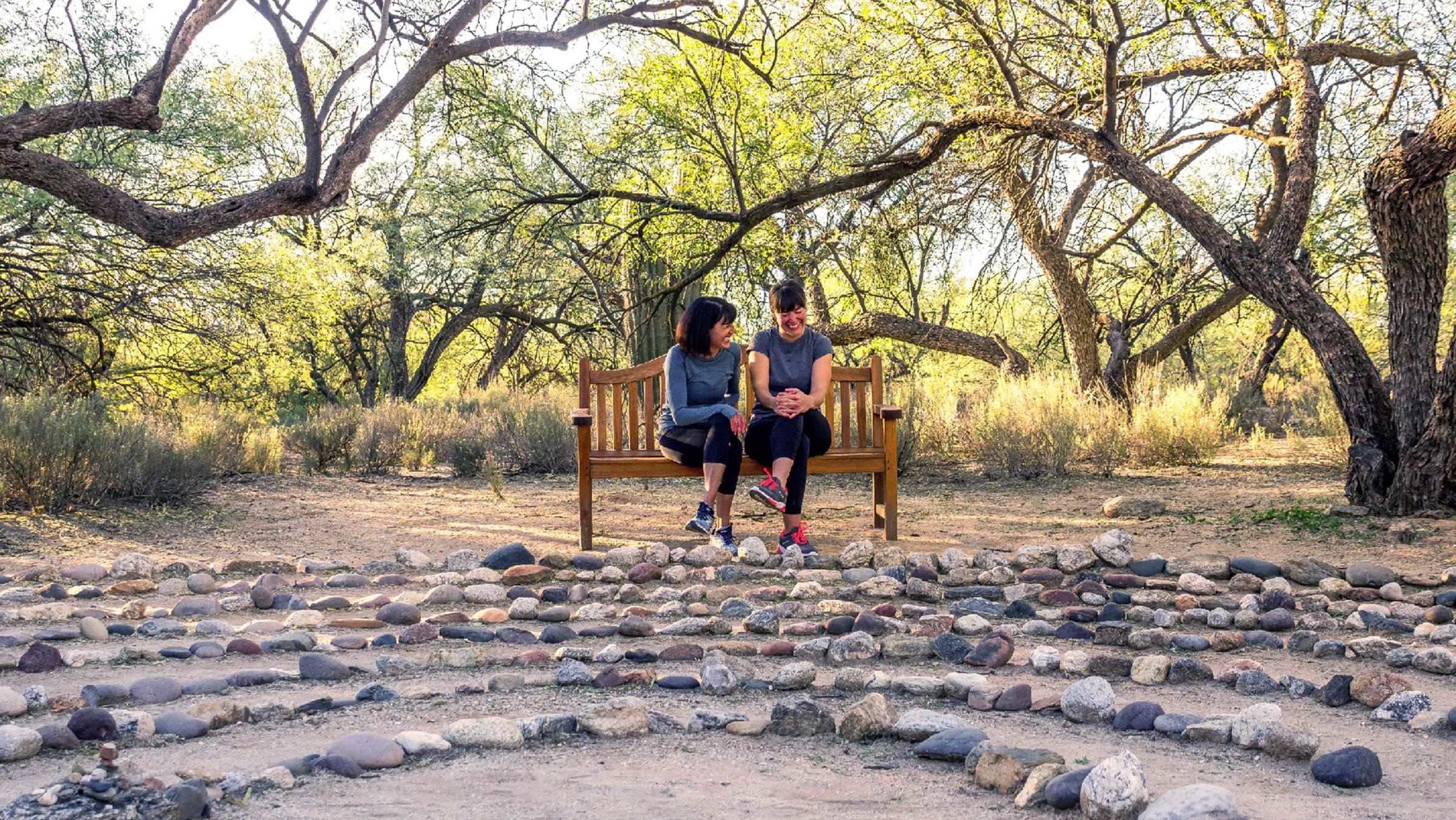 Mother and daughter sitting on wooden bench outside facing a stone labyrinth.