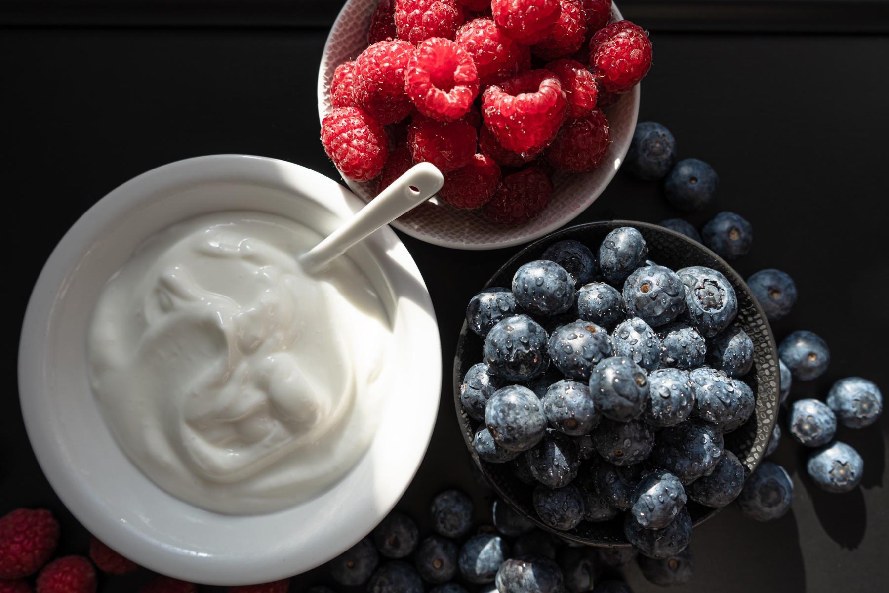 Close-up overhead shot of a bowl of yogurt next to a bowl of raspberries and a bowl of blueberries.