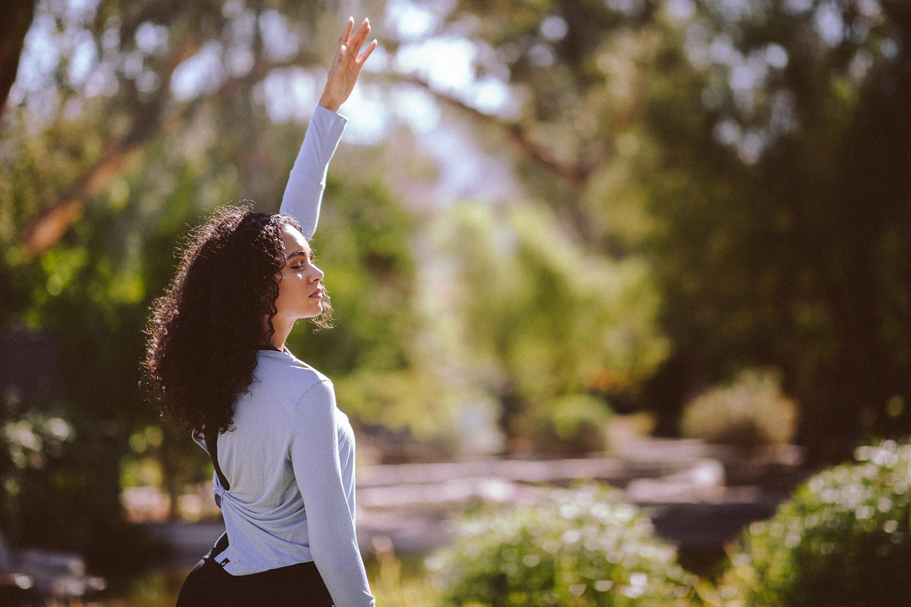 Woman smiling outside with arm raised in air.