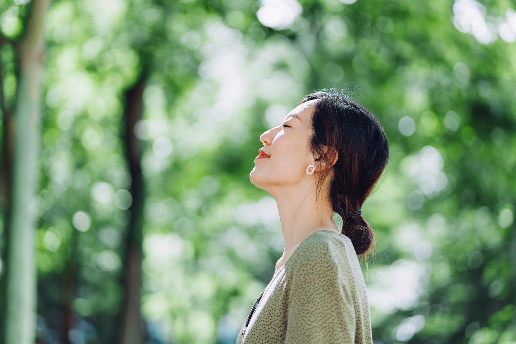 A young woman in the woods looking up at the sky in thought.