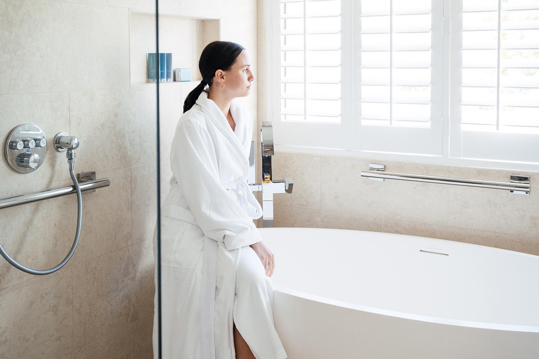 A woman standing in a Canyon Ranch Tucson suite bathroom next to the bathtub.