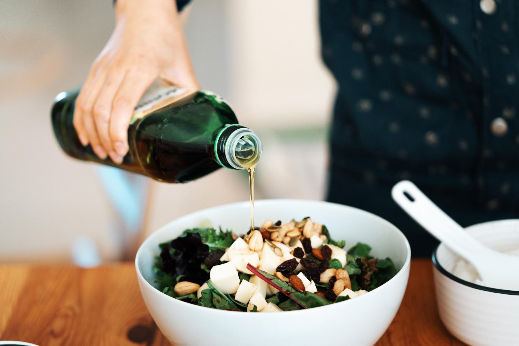 woman's arm pouring olive oil onto bowl of salad