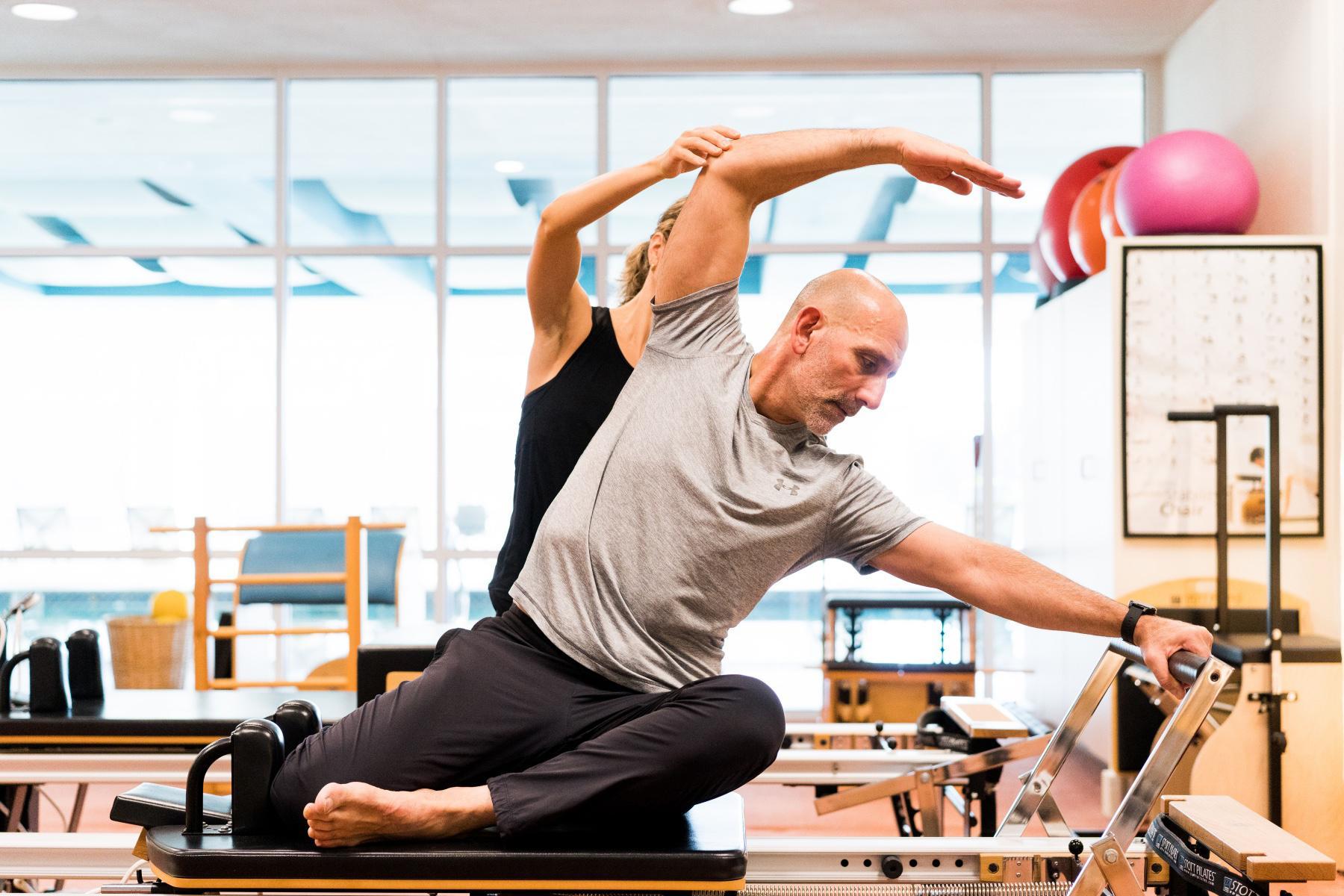 man being guided on pilates reformer machine by woman behind him
