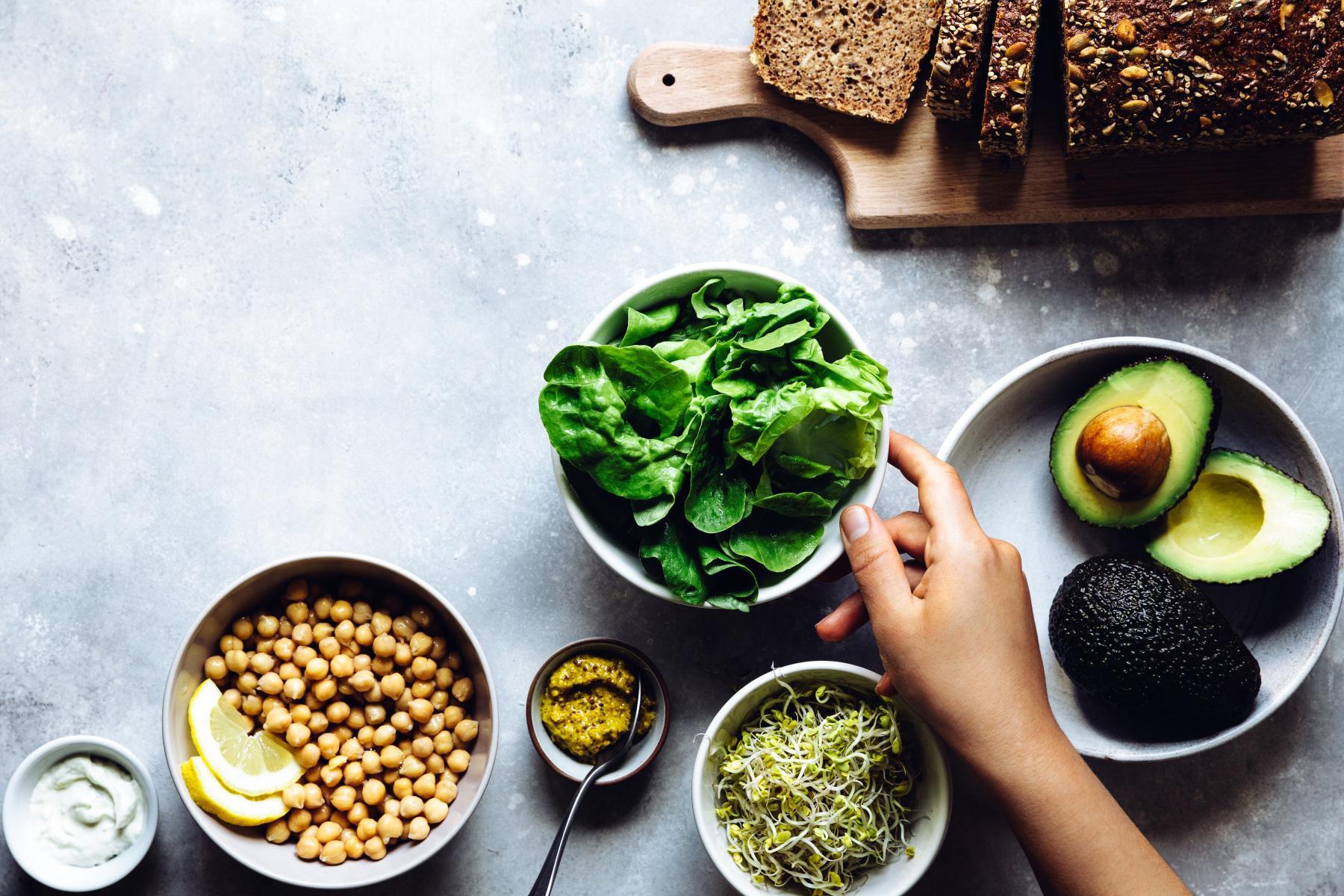 overhead image of a bowl of spinach, a bowl of chickpeas, and a load of healthy bread on cutting board