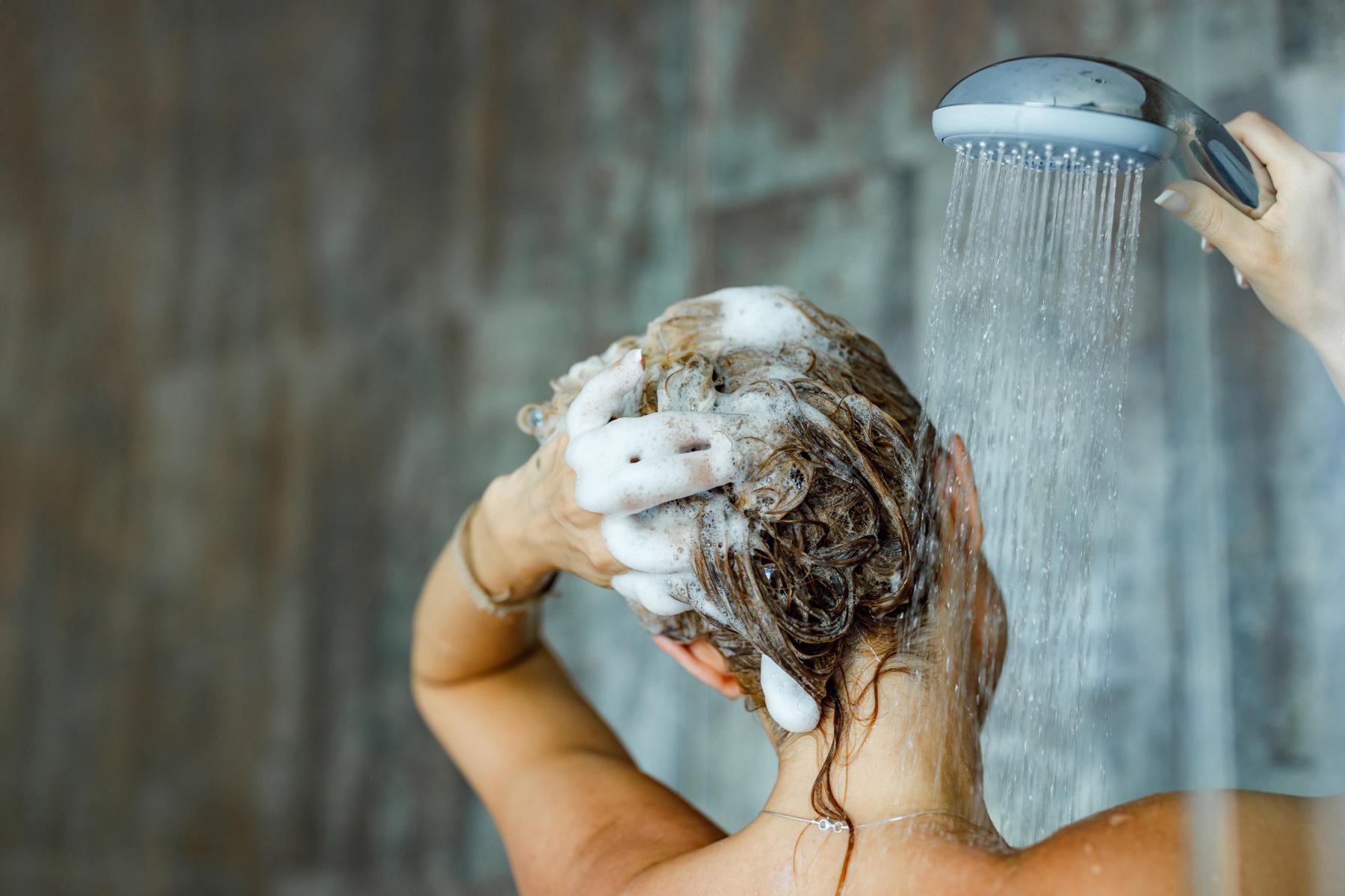 A woman washing her hair with shampoo in the shower.