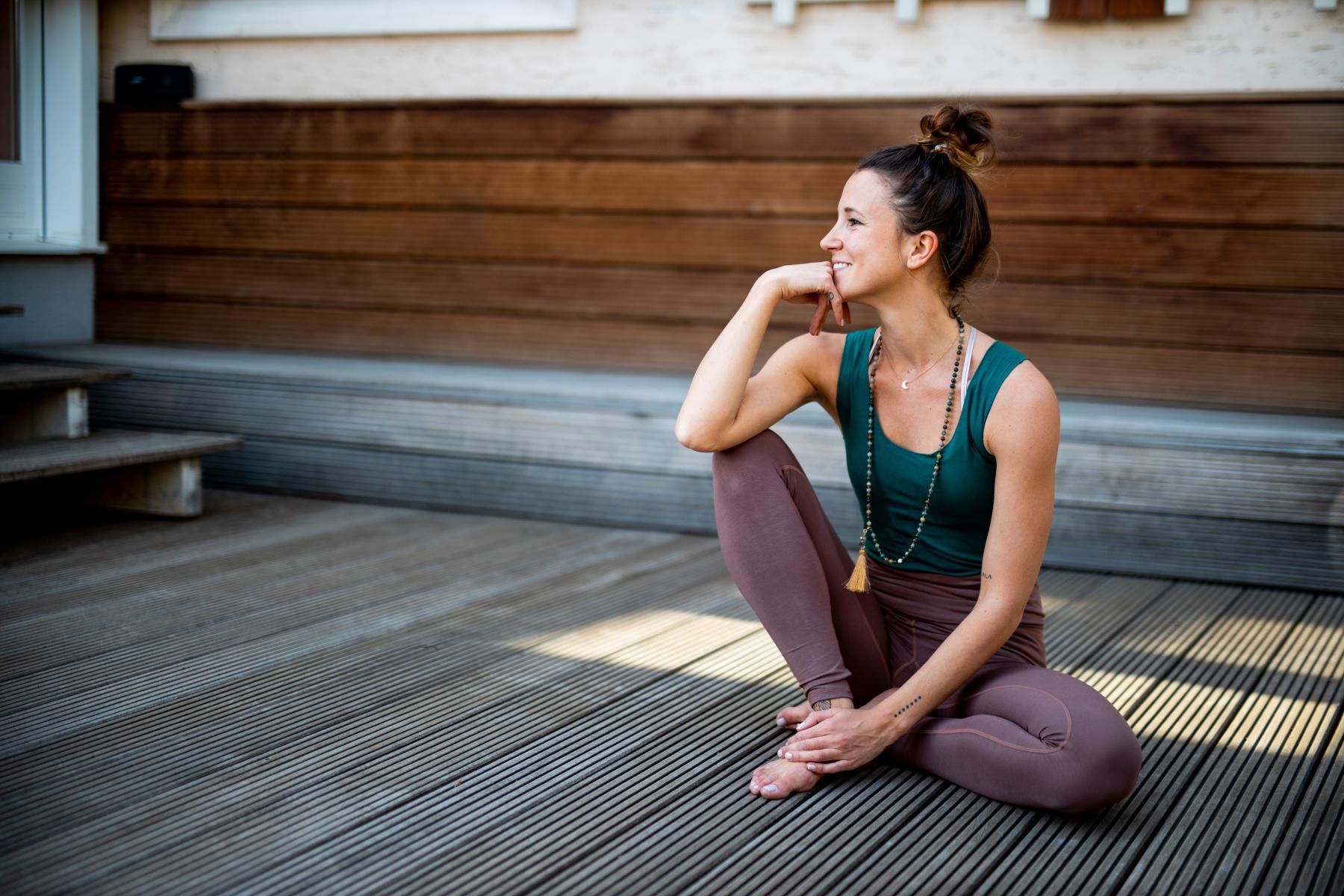 Woman sitting outside on floor of deck after yoga practice smiling and looking off to the side.