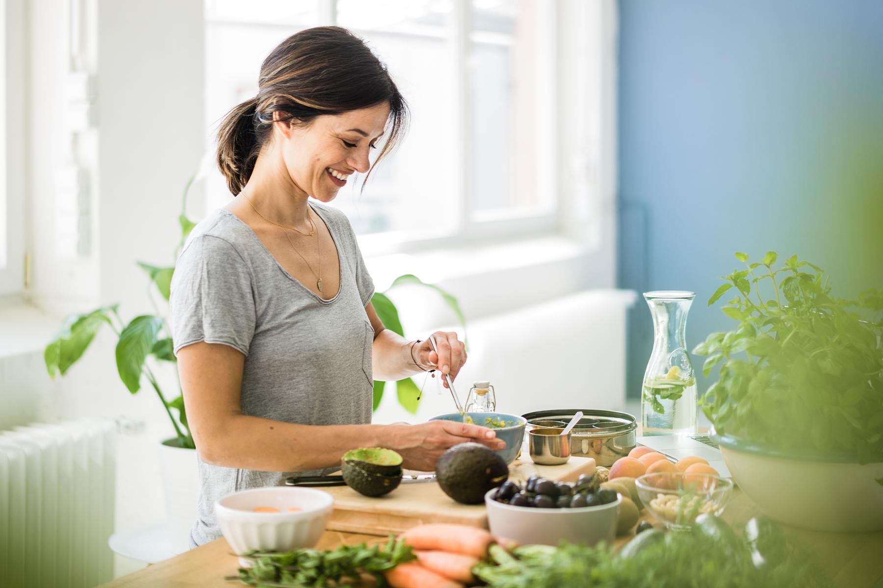 woman smiling from size while making guacamole in bright kitchen