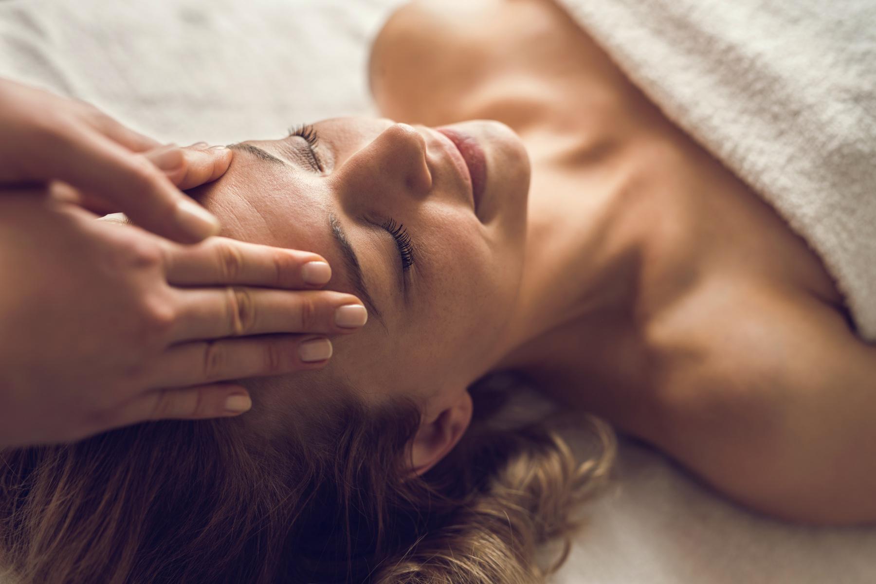 Close-up of woman's face with hands gently pressing on her forehead.