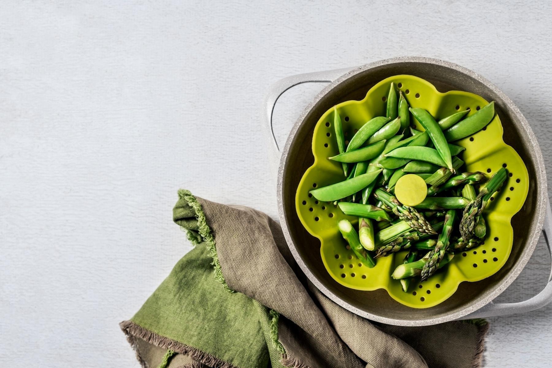 Overhead view of peas in a green vegetable steamer.