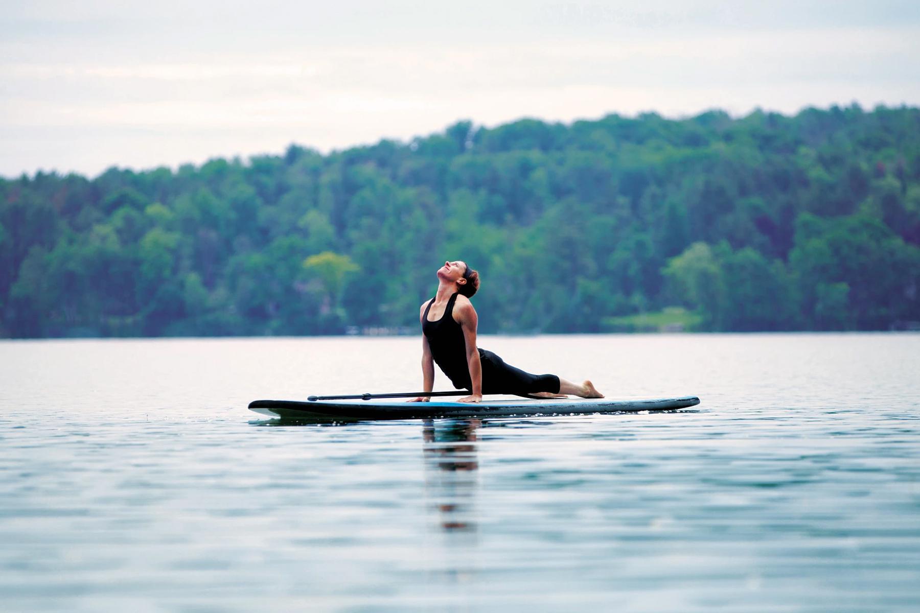 woman floating on paddle board in lake while doing sphinx yoga pose