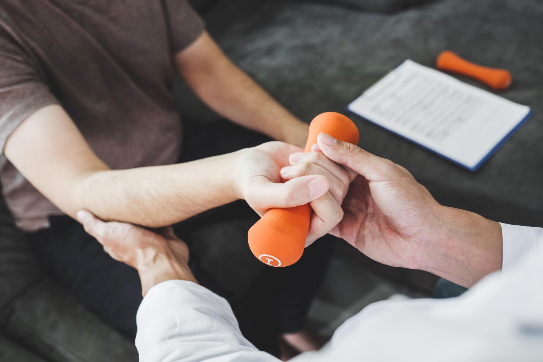 Close-up on man receiving assistance from a physical therapist as he curls a 1 pound orange dumbbell.