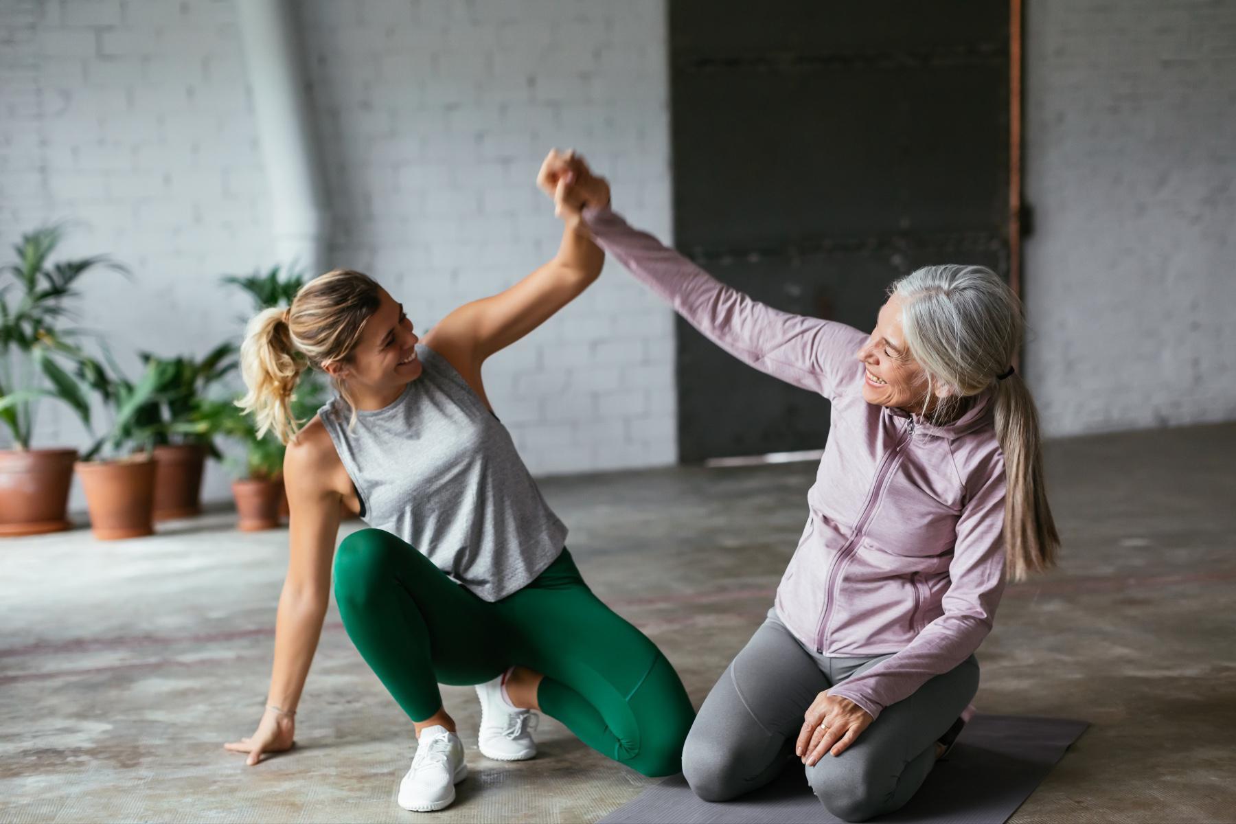 two women mid workout kneeling on the ground and holding their hands together in the air in celebration