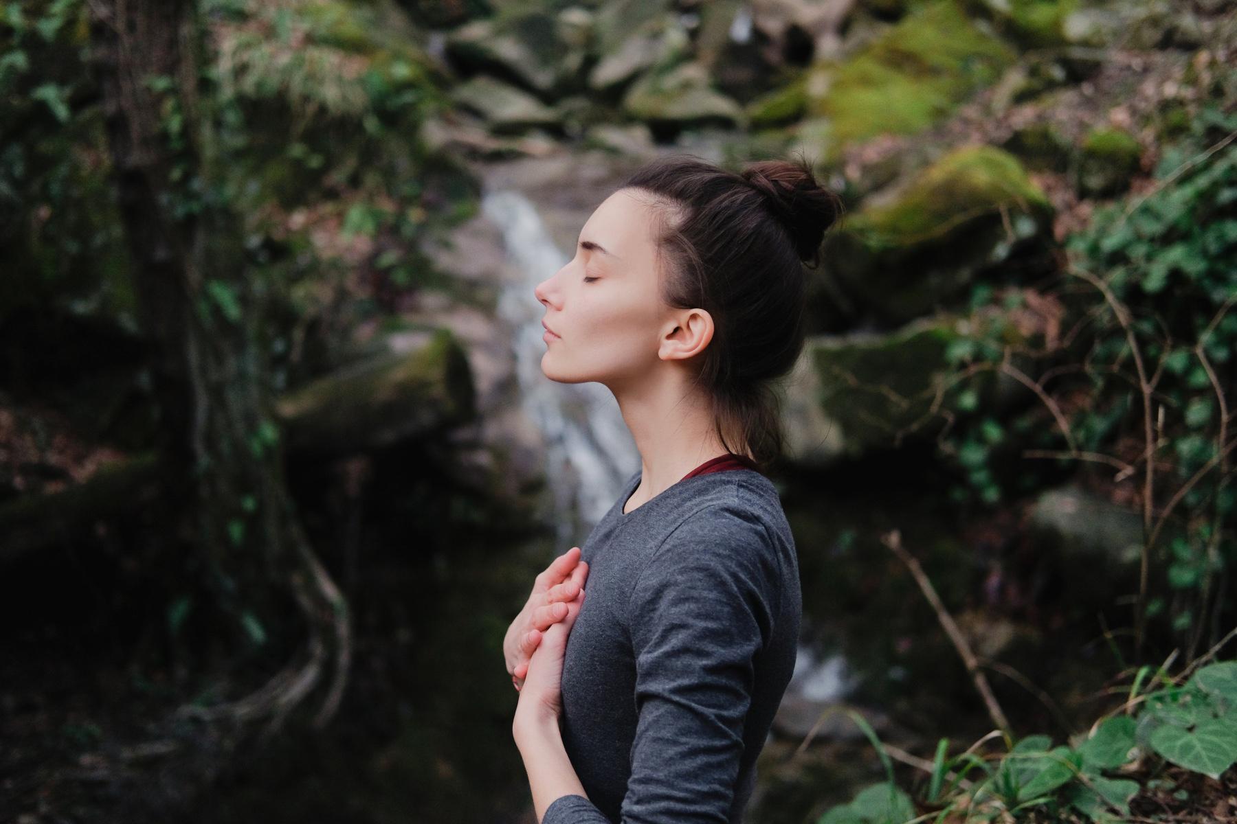 Woman standing in the forest with her eyes closed.